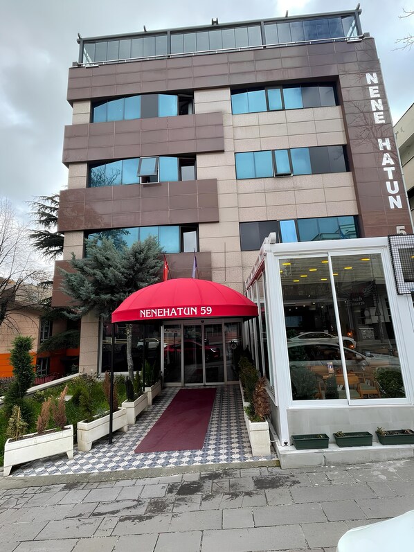 Une entrée d’hôtel moderne avec un parasol rouge, des portes vitrées et un trottoir dallé.