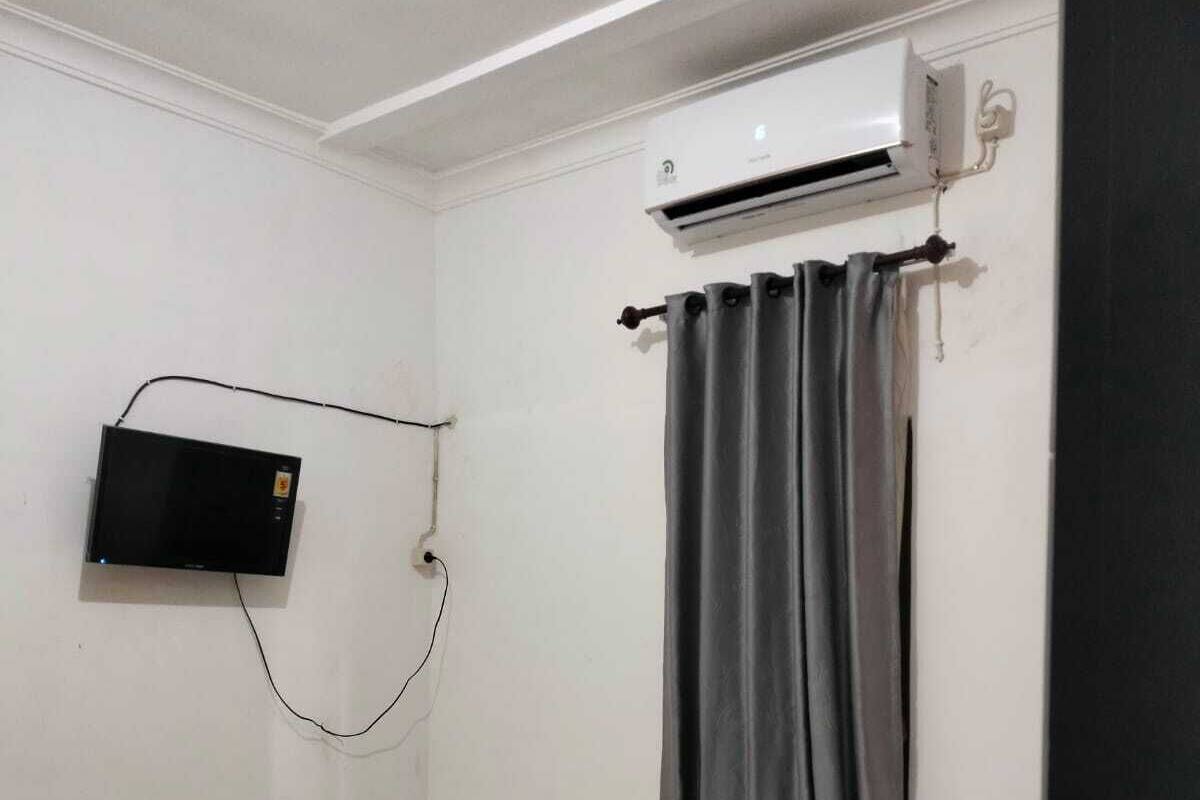 Ein Hotelzimmer mit einem Bett, einem an der Wand montierten Flachbildfernseher und einer Klimaanlage über dem Fenster.