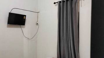 A hotel room with a bed, a flat-screen TV mounted on the wall, and an air conditioning unit above the window.