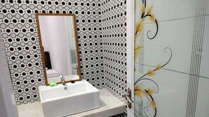 A bathroom with a white sink, a mirror with a wooden frame, and patterned walls. - galtri homestay (Banyuwangi)