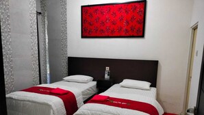 A hotel room with two beds, each with a white bedspread and a red blanket. There is a red decorative wall hanging above the beds. - galtri homestay (Banyuwangi)
