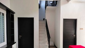 A hallway with a staircase, a black door, and a red table. - galtri homestay (Banyuwangi)