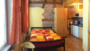 Une chambre comprenant un lit, une chaise en bois, une armoire et un coin cuisine équipé d’un four à micro-ondes.