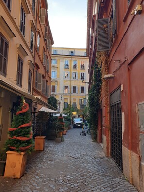 A narrow cobblestone street flanked by buildings with balconies and shutters, leading to a building with a sign that reads "Caffetteria." - Cozy and comfortable, Trevi Fountain. For families, max 6 guests. AC WIFI (ROMA)