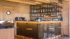 Un espace bar avec un comptoir en bois, des tabourets, une machine à café et un présentoir à bouteilles de vin.