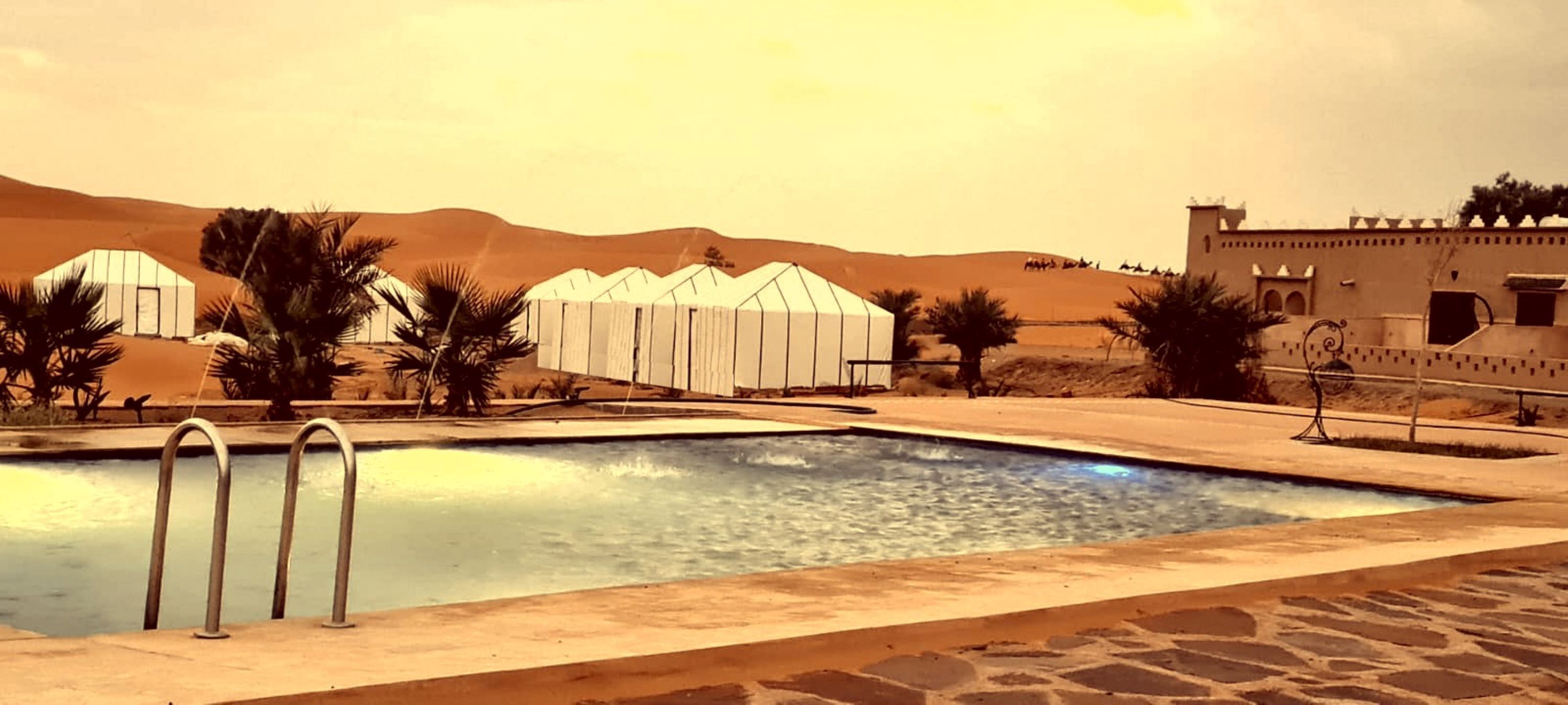 A pool area with a clear view of the surrounding landscape, including tents and a building with traditional architecture.
