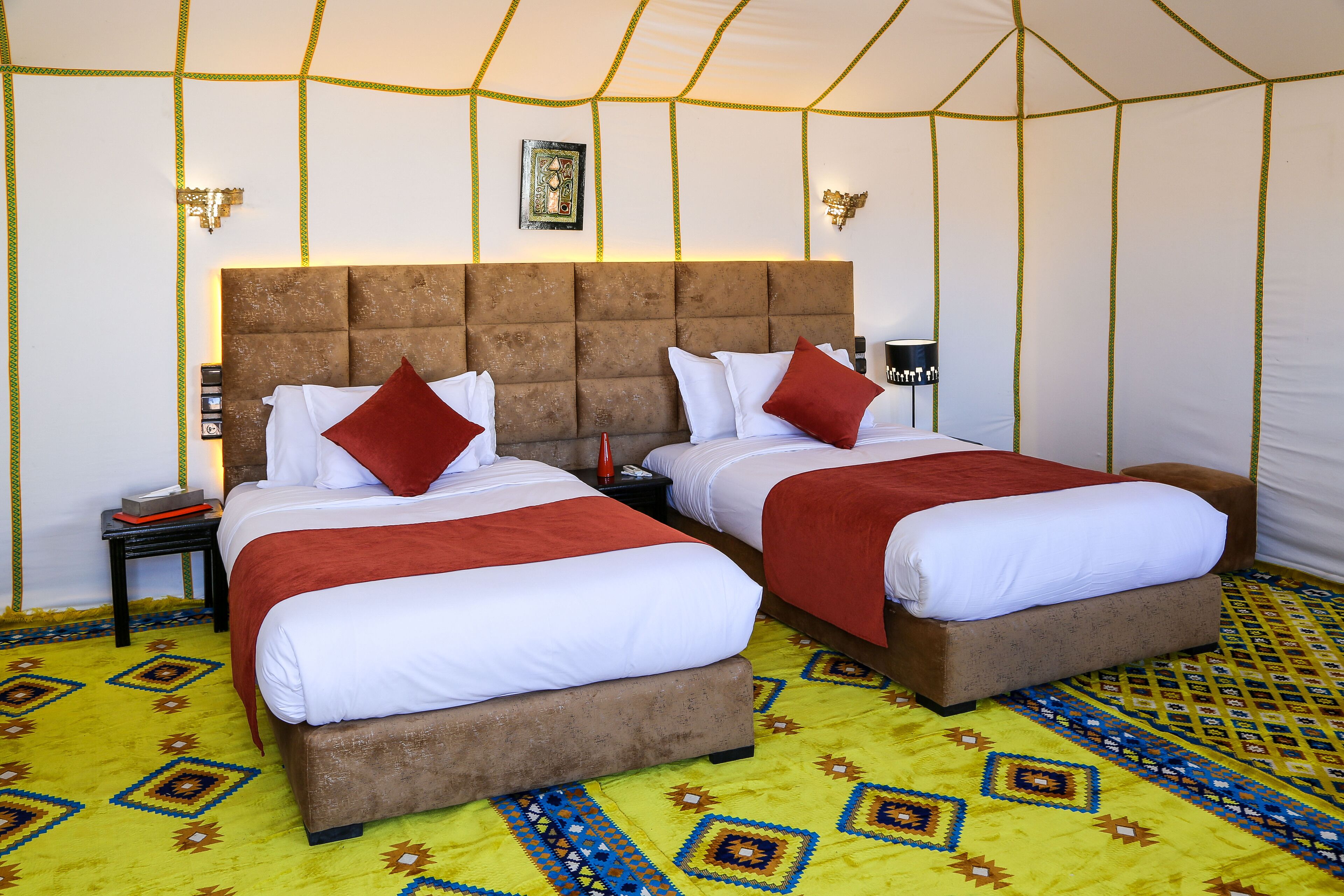 A tent-style room with two beds, each with white bedding and red pillows, and a patterned carpet.