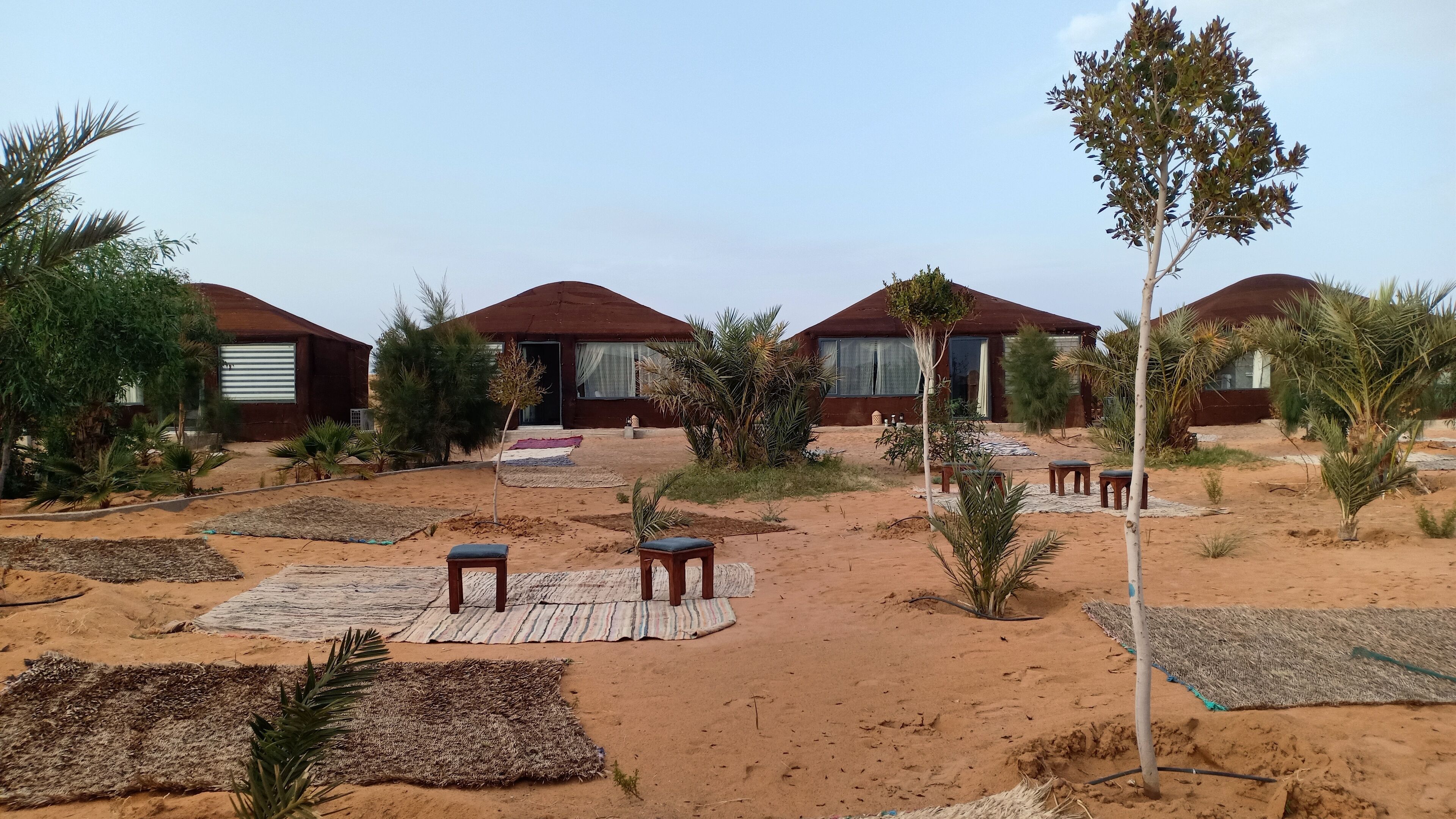 Een woestijnesort met verschillende accommodaties in de stijl van bungalows, elk met een overdekt terras en een kleine tuin.