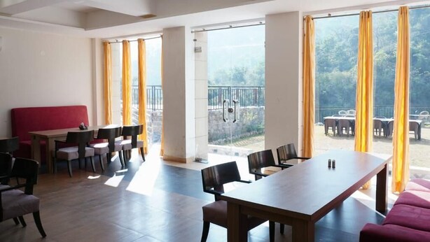 Un amplio espacio interior con una larga mesa y sillas, un sofá rojo y ventanas grandes con cortinas.