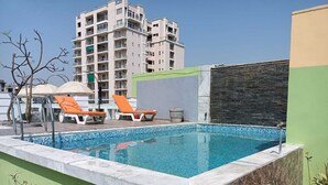 Una piscina con sillas de descanso, un muro de piedra y un edificio de varios pisos al fondo.
