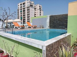 Una piscina con sillas de descanso, un muro de piedra y un edificio de varios pisos al fondo.