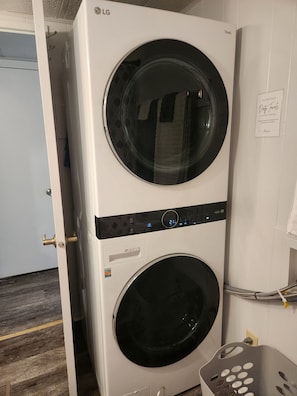 A stacked LG washer and dryer unit in a room with a wooden floor and white walls.