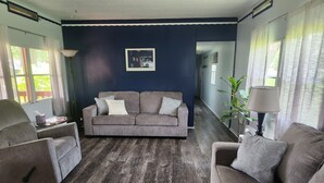 Una sala de estar con una pared azul oscuro de acento, un sofá gris con cojines estampados, piso de madera y una lámpara.