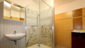 Een badkamer met een douchecabine van glas, een wastafel en een meubel met een spiegel.