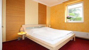Een net opgemaakt bed in een kamer met een houten hoofdbord, een bedlampje en een raam met uitzicht op groen.