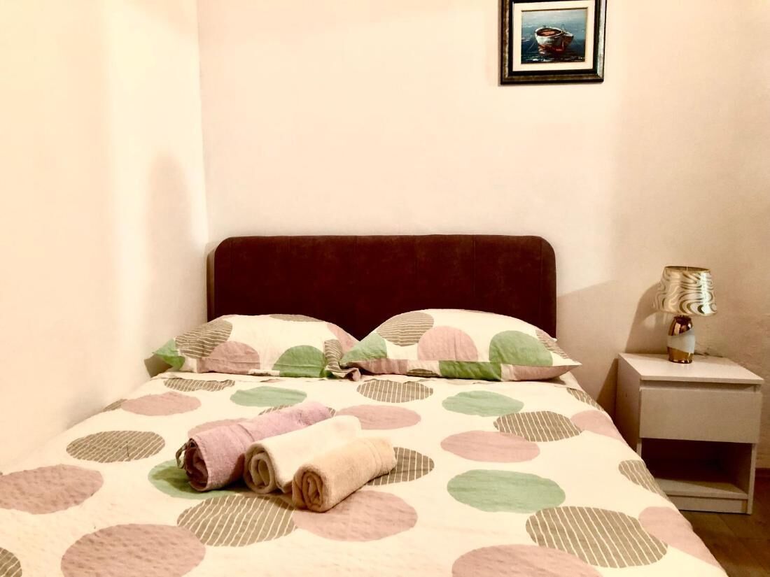 A bed with a polka dot bedspread, a rolled towel, a nightstand with a lamp, and a framed picture on the wall.