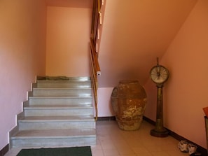 Een trap met een leuning, een grote keramieken pot en een klok aan de muur.