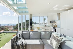 Un soggiorno moderno con un divano grigio, un soffitto in vetro e vista sulla città.