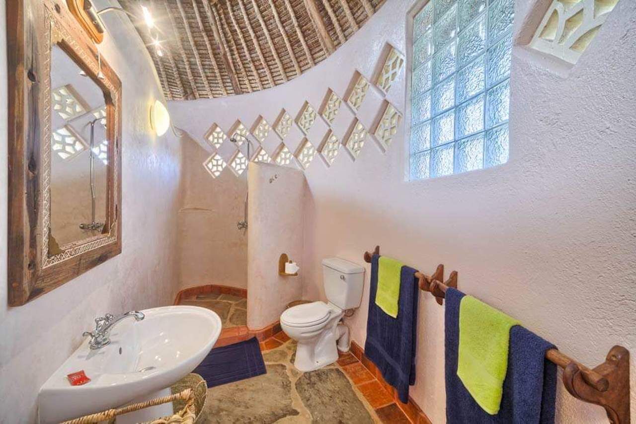 A bathroom with a stone floor, a white sink, a toilet, and a shower area.