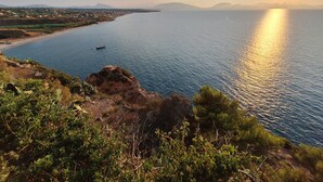 Un paysage côtier offrant une vue dégagée sur la mer, avec un bateau et des montagnes  à l’horizon.