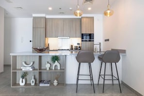 A modern kitchen with a central island, two bar stools, and pendant lighting. - Brand New Apt Modern 1br Amazing Marina Views (Dubai)