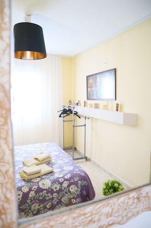 Ein Hotelzimmer mit Bett, einer Hängelampe, einem Kleiderständer und einem Regal mit Dekorationsgegenständen.