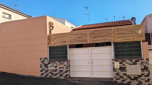 Un immeuble résidentiel avec un toit recouvert de tuiles, une entrée fermée par un portail et une petite fenêtre ornée d’une grille métallique.