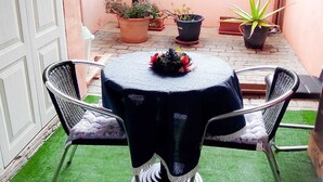 Une petite terrasse extérieure avec une table ronde et deux chaises, entourée de plantes en pot.