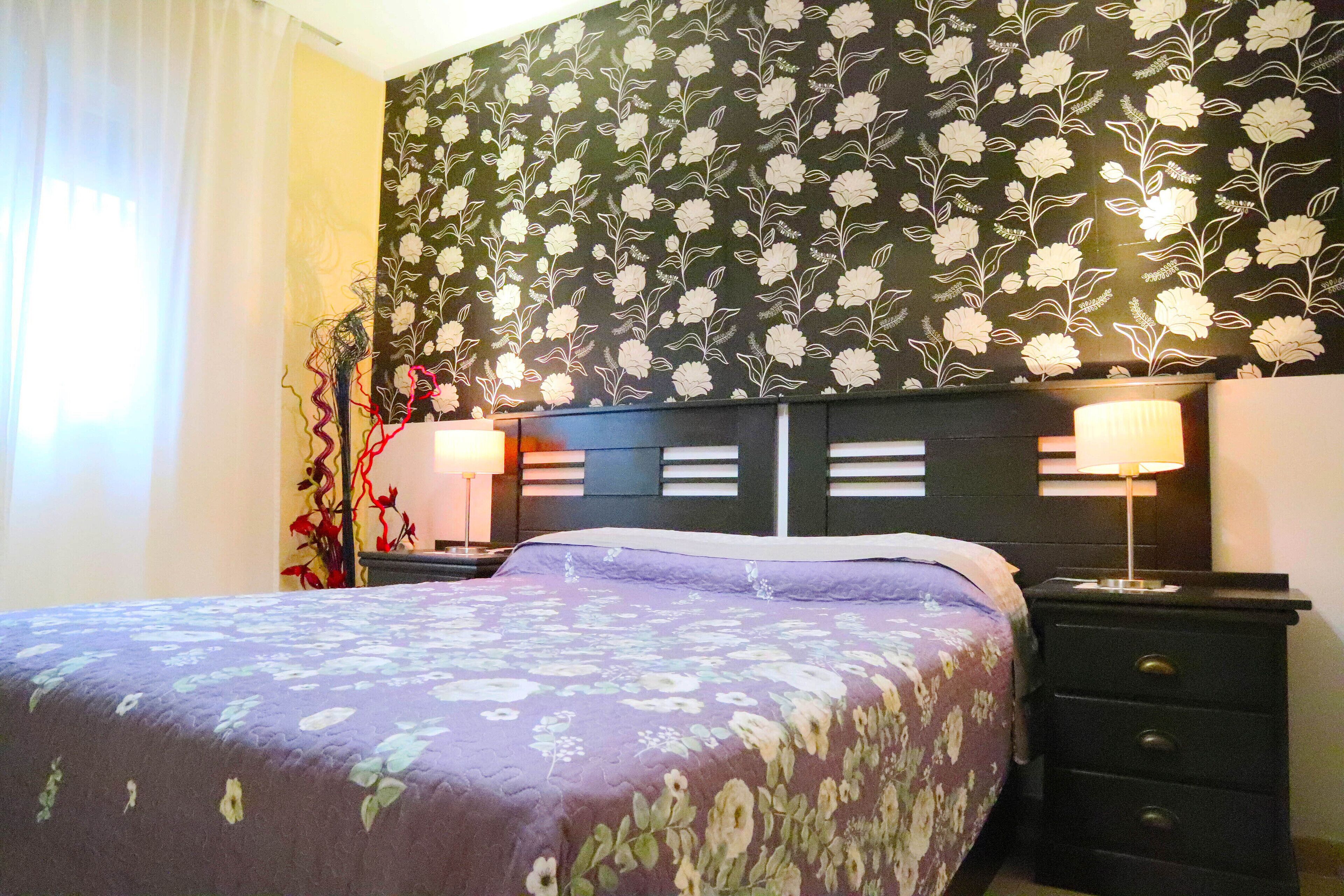 Une chambre d ’hôtel avec un lit, deux tables de chevet et un papier peint à motifs floraux.
