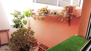 Un petit balcon agrémenté de plantes en pot et d’une zone recouverte d’un gazon synthétique vert.
