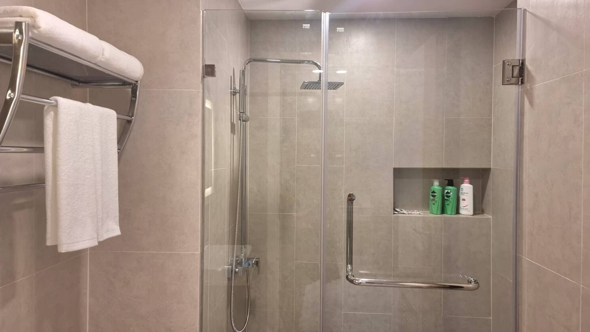 A modern shower area with a glass enclosure, a towel rack, and a shelf with toiletries.