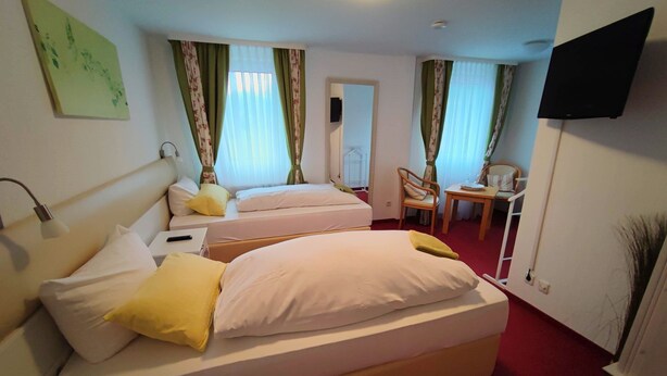 A hotel room with two beds, a desk, a chair, and a TV mounted on the wall. - Room in Guest Room - Pension Forelle - Double Room (Forbach)