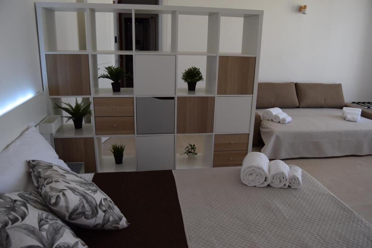 Una camera d'albergo con un letto, una poltrona, un tavolino con una pianta e un mobile contenitore con scaffali.