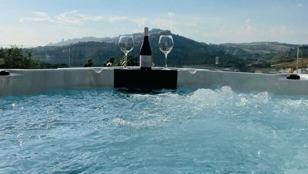 Un bain à remous avec une bouteille et des verres sur une table, offrant une vue sur un paysage montagneux.