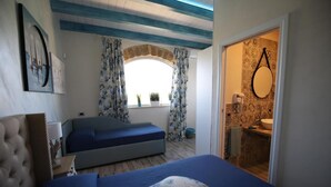 Une chambre avec un lit, une fenêtre avec des rideaux, une salle de bain avec un lavabo et un miroir, et un petit balcon.