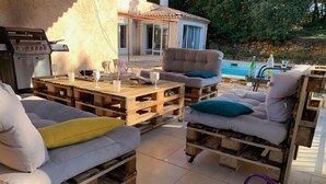 Een terras met een zwembad, tuinmeubels van pallets en een barbecue.