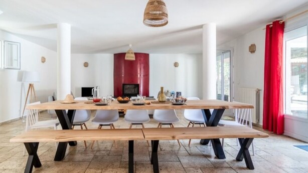 Een eetruimte met een lange houten tafel, witte stoelen en een rode accentmuur.