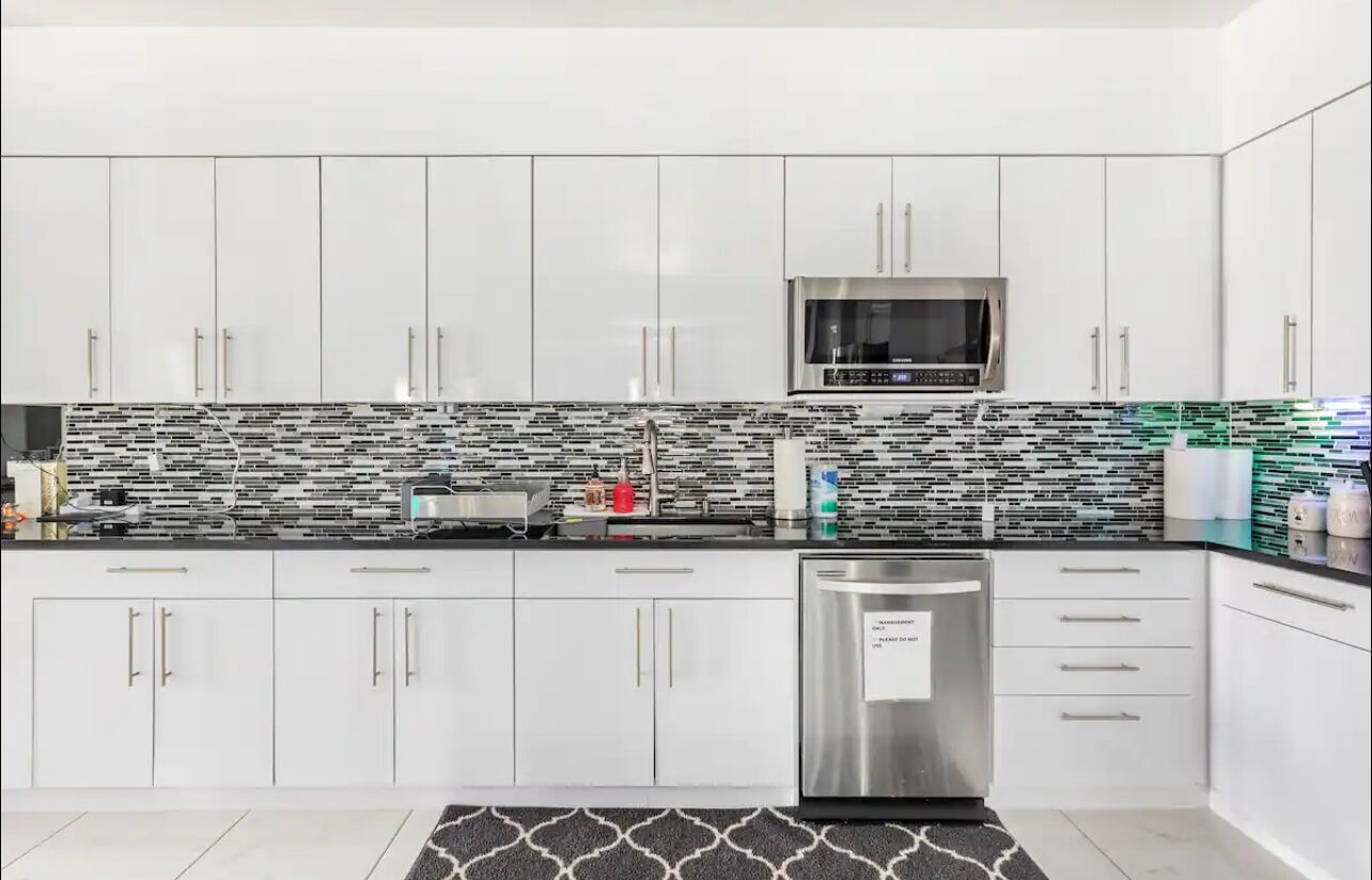 Uma cozinha moderna com armários brancos, micro-ondas de aço inoxidável e painel de fundo padronizado.