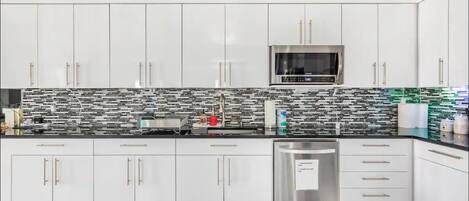 Uma cozinha moderna com armários brancos, micro-ondas de aço inoxidável e painel de fundo padronizado.