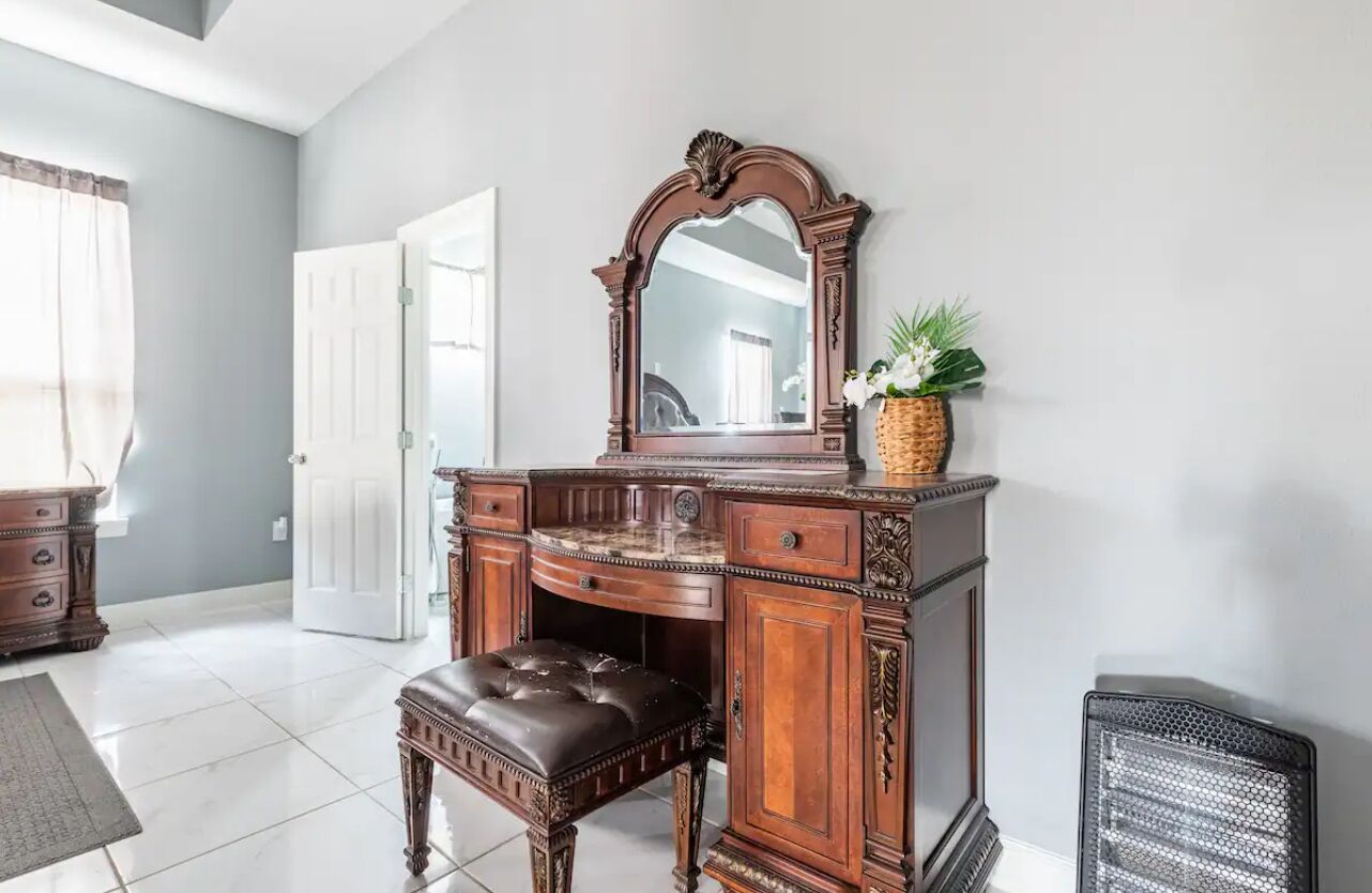 A traditional wooden dresser with a mirror, a bench, and a wicker basket with flowers.