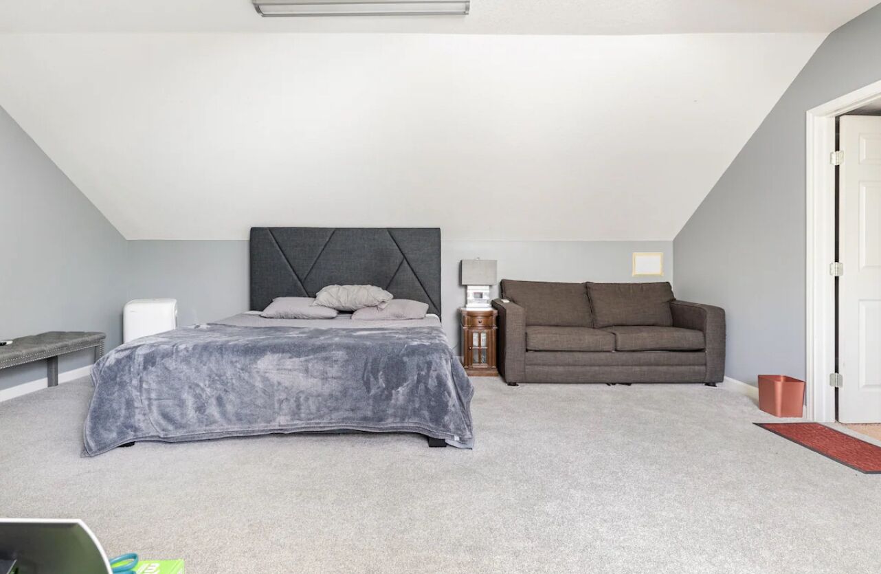 A bedroom with a bed, a gray headboard, a gray couch, a nightstand, and a door.
