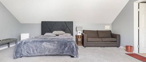 A bedroom with a bed, a gray headboard, a gray couch, a nightstand, and a door.