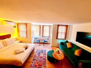 Quarto de hotel com cama, sofá, mesa pequena e televisão.