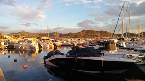 A marina with boats docked, calm water, and a hilly landscape in the background.