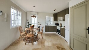Une cuisine avec un coin repas, comprenant une table ronde, des chaises, un luminaire suspendu et un réfrigérateur.