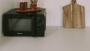 Une cuisine avec un four à micro-ondes posé sur le comptoir, une planche à découper en bois et un petit récipient en bois contenant des ustensiles.
