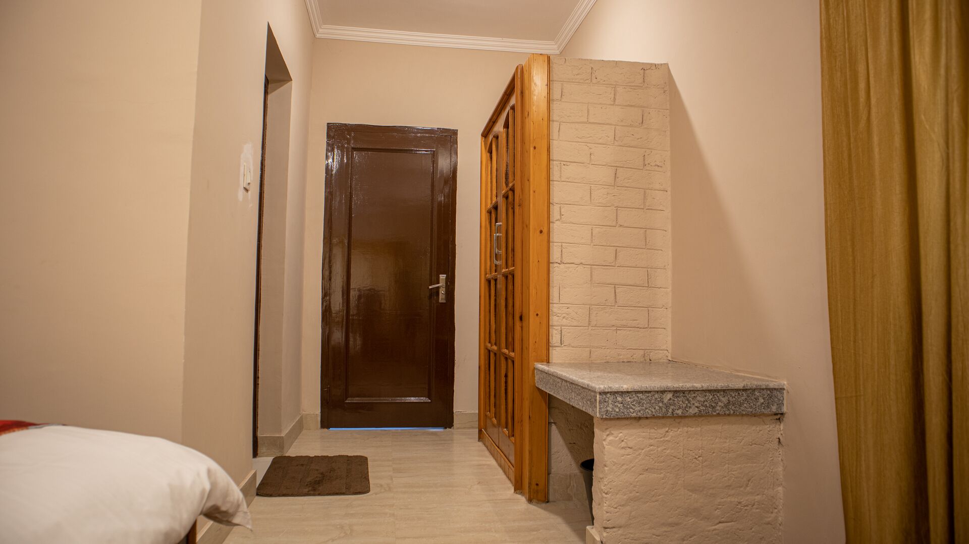 Un pasillo estrecho con una puerta de madera, un banco de piedra y una cama con almohada blanca.