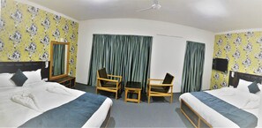 Habitación de hotel con dos camas, un escritorio, dos sillas, un televisor y cortinas.