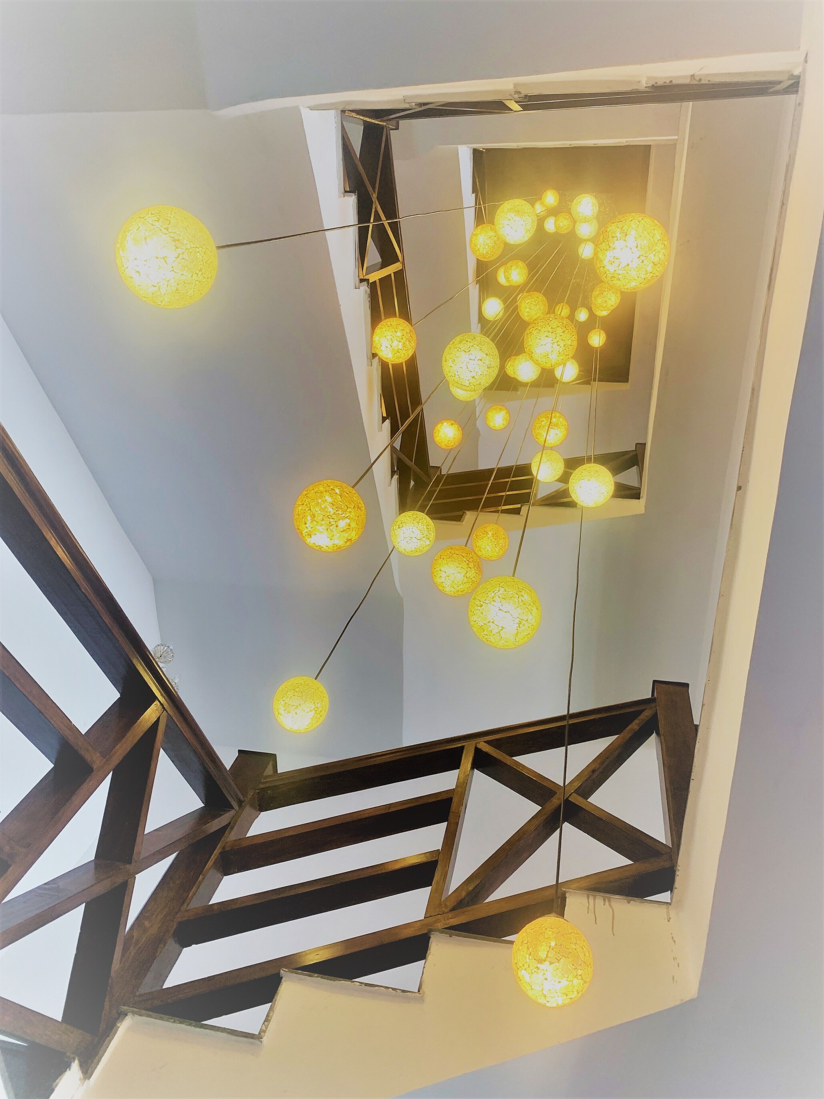 Uma escadaria com corrimãos de madeira e luminárias esféricas suspensas.