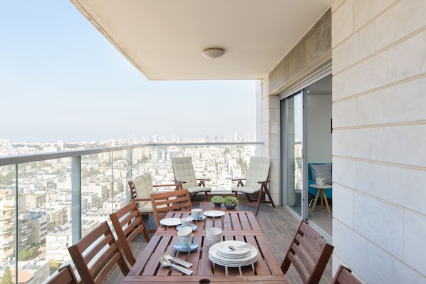 A balcony with a table set for dining, chairs, and a city view.